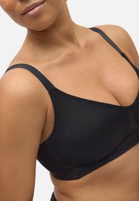 Sujeta negra con diseño de lunares texturizados, tirantes ajustables y detalles de malla transparente en los copas, que ofrece una silueta suave.