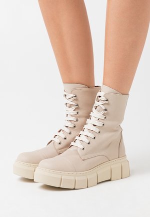 Beige combat boots with a high shaft, lace-up front, and chunky beige rubber sole. Smooth texture and rounded toe design.