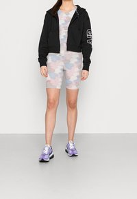 Černá kratká mikina s předními kapsami; šedé a pastelově maskáčové šortky na kolo; fialové tenisky s bílými tkaničkami a černou podrážkou.