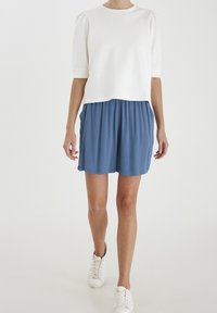 Biały top z krótkim rękawem w duecie z niebieskimi plisowanymi szortami i białymi trampkami; luźny fason, teksturowana tkanina i subtelne detale designu.