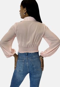 Crop top sheer di colore rosa chiaro con maniche a palloncino e elastico in vita, abbinato a jeans in denim blu a vita alta con tasche posteriori.
