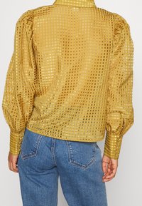 Blouse à carreaux jaunes en tissu transparent, manches bouffantes et détails de boutons aux poignets. Associée à un jean en denim bleu.