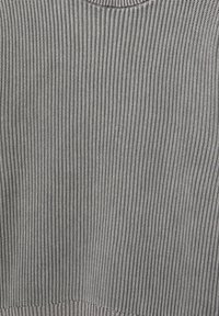 Grå ribbad stickad tröja med en texturerad yta och rundad halsringning. Tyget har en medeltjocklek och konsekventa vertikala linjer.