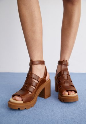 Hnědé kožené sandály na podpatku se tkaným designem, otevřenou špičkou, řemínkem na kotníku a masivní platformou s texturovanými akcenty.