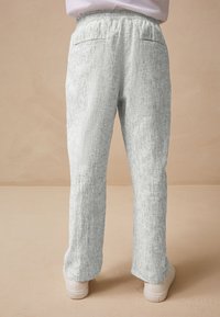 Pantalon gris clair texturé avec une taille élastique et deux poches. Les jambes sont droites et s'arrêtent juste au-dessus de chaussures blanches.