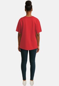 T-shirt rosso a maniche corte, vestibilità comoda, scollatura rotonda, abbinato a jeans skinny scuri e sneakers bianche. Tessuto semplice e liscio.