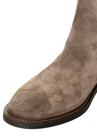 Braune Wildleder-Ankle Boots mit einer glatten Textur, runder Zehenpartie und einer kontrastierenden dunklen Sohle; Sichtbare Nähte entlang der Kante der Sohle.