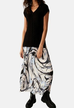 Sort kabelstrikket kortærmet top, kombineret med en plisseret maxinederdel i hvid, blå og sort hvirvelmønster, fuldendt med chunky sorte støvler.