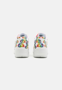 Sneaker bianche con grafiche a cuore arcobaleno sui lati, collo imbottito e suole in gomma testurizzata. Accenti rossi vicino alla parte superiore.