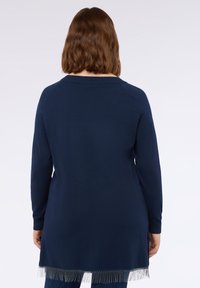 Maglione blu navy a maniche lunghe con scollatura tonda, spacchi laterali e dettagli in frange all'orlo. Texture morbida e design aderente.