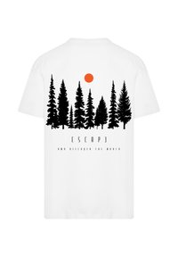 White cotton t-shirt featuring a graphic of black pine trees and an orange circle resembling a sun. Text reads "ESCAPE AND DISCOVER THE WORLD."
