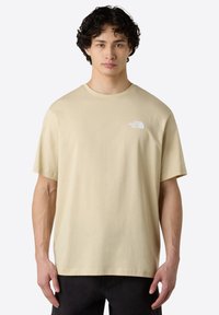 Béžové bavlněné tričko s krátkým rukávem a kulatým výstřihem. Obsahuje malé bílé logo na levé části hrudi. Rovný lem a volný střih.