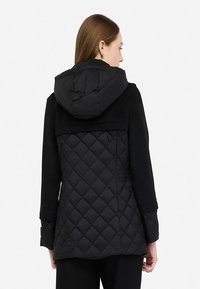Giacca nera trapuntata con cappuccio e un corpetto liscio, realizzata con un mix di materiali e una vestibilità rilassata. Sul retro presenta una texture contrastante.