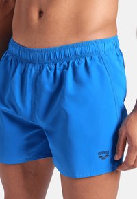Pantaloni da mare blu realizzati in tessuto leggero, con vita elastica e dettagli del logo esterno, caratterizzati da un design semplice e una consistenza liscia.