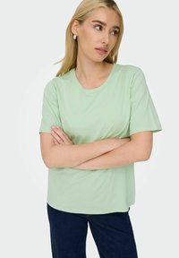 Mintgrøn t-shirt lavet af blødt bomuld, med rund halsudskæring og korte ærmer, parret med mørkeblå jeans.