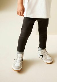 Leggings negre cu dungi, tricou alb și adidași gri cu accente albe și negre; design low-top și talpă texturată.
