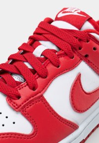 Piros és fehér tornacipő sima bőr felsőrésszel, piros textil fűzőkkel, perforált orral és egy feltűnő fehér Nike logóval.