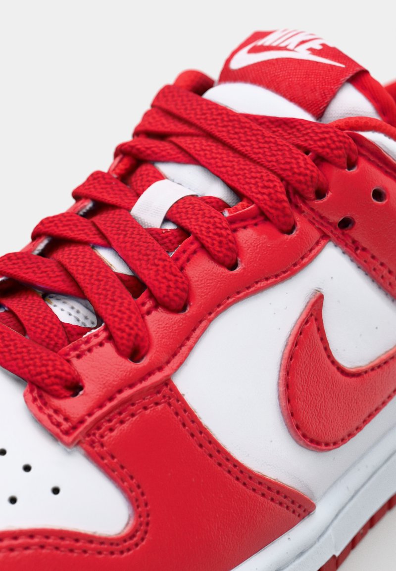 Baskets rouges et blanches avec une tige en cuir lisse, des lacets en textile rouge, une pointe perforée et un logo Nike blanc bien en vue.