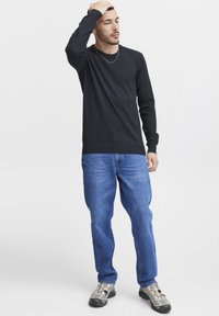 Mörkgrå långärmad tröja med ribbad krage, i kombination med blå jeans och grå sneakers med nätaccenter och snörning.