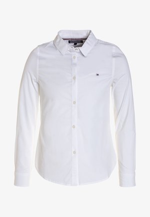 Biała koszula z długim rękawem, kołnierzykiem, zapinana na guziki i z małym logo Tommy Hilfiger po lewej stronie klatki piersiowej.