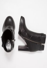 Botas de cuero negro hasta el tobillo con cremallera lateral, punta redonda y tacón en bloque apilado. Textura suave con un acabado pulido.