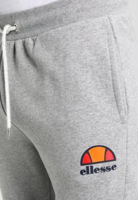 Pantalones de chándal grises de material suave, con una cinturilla acanalada, bolsillos laterales y un logotipo colorido con acentos en naranja y rojo.