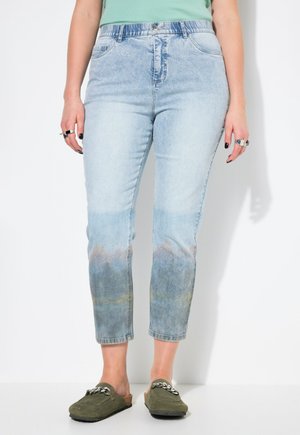 Jeans en denim bleu clair avec un effet dégradé délavé, taille haute et longueur crop. Assortis à des chaussures olive à enfiler.