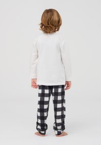 Biała polarowa bluzka z długim rękawem połączona z czarno-białymi sztruksowymi spodniami do piżamy w kratkę. Miękka tekstura i luźny krój, zaprojektowane z myślą o komforcie.