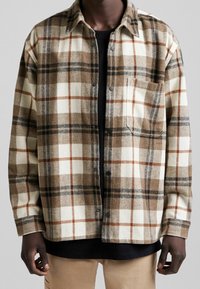 Brązowa i kremowa koszula flanelowa w kratę z dużymi kwadratami, z kieszenią na piersi i zapięciem na guziki. Miękka tekstura, z kołnierzykiem.