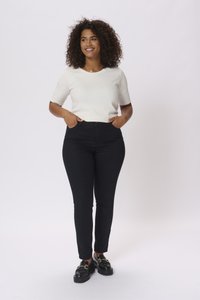 Jeans skinny neri a vita alta con una finitura liscia, abbinati a un top fitted a maniche corte di colore crema. Mocassini neri con dettagli dorati.