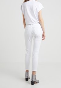 Bílé skinny džíny s hladkou texturou, s klasickými zadními kapsami. Nosí se s metalickými kotníkovými botami a obyčejným bílým tričkem.