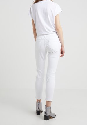 Valkoiset kapeat farkut, joissa on sileä pinta ja tavalliset takataskut. Yhdistetty metallinhohtoisilla nilkkabootseilla ja yksinkertaisella valkoisella T-paidalla.