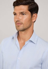 Lichtblauw geruit overhemd met een zachte textuur, button-down kraag en korte placket met witte knopen. De stof lijkt glad te zijn.