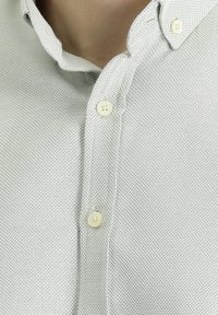 Camicia grigia chiara con texture, dotata di colletto button-down e quattro bottoni beige lungo la placket anteriore.