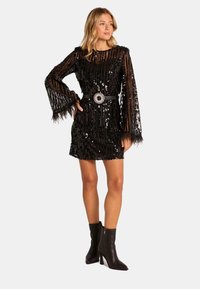 Abito mini nero in sequins con maniche a campana lunghe, dettagli in piume e una larga cintura nera con una fibbia metallica circolare.