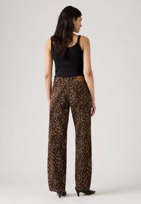 Bruine dierenprint wijde broek met een hoge taille. Katoenen stof met een gestructureerd oppervlak. Zwart tanktop en hoge hakken worden gedragen.