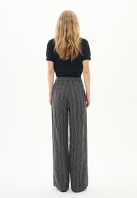 Gestreifte, weit geschnittene Hose in Schwarz und Weiß aus strukturiertem Stoff, mit hohem Bund und Gesäßtaschen. Modell trägt ein schwarzes Shirt.