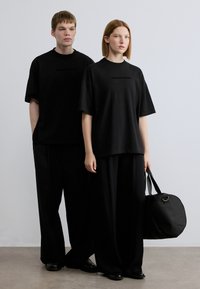 Μαύρα oversized t-shirt με λογότυπο, μαύροι φαρδιοί παντελόνες και μαύρη τσάντα. Απλός σχεδιασμός με απαλή υφή και μινιμαλιστικό στυλ.