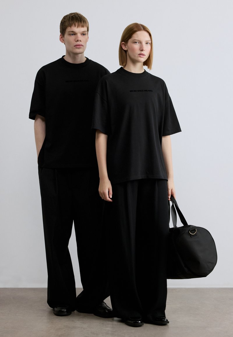 Μαύρα oversized t-shirt με λογότυπο, μαύροι φαρδιοί παντελόνες και μαύρη τσάντα. Απλός σχεδιασμός με απαλή υφή και μινιμαλιστικό στυλ.