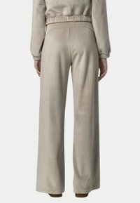 Pantaloni a gamba larga in morbido tessuto beige, caratterizzati da una texture liscia e vita alta. La cintura elastica presenta dettagli arricciati.