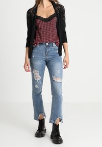 Czarny koronkowy kardigan na czerwonej i czarnej kraciastej koszulce na ramiączkach, w połączeniu z postrzępionymi niebieskimi dżinsami i czarnymi botkami.
