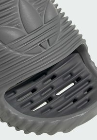 Gray slide sandal made of textured rubber. Features ribbed design and cut-out holes for breathability, with an embossed logo on the strap.