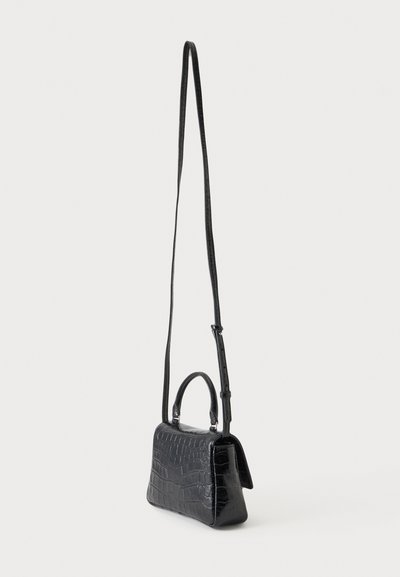 Petit sac à main noir à texture crocodile, poignée courte et longue bandoulière réglable sur fond blanc.