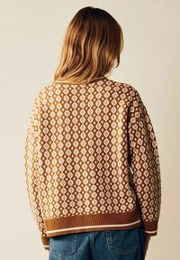 Brun och krämfärgad mönstrad tröja med diamantdesign och ribbad nederkant. Har en löst sittande passform och texturerat stickat material. Bakvy visas.