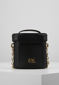 Schwarze Lederhandtasche mit quadratischer Form, Kettenriemen, oberem Griff, Fronttasche und goldfarbener Logodetaillierung. Glatte Textur und minimalistisches Design.