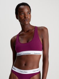 Burgundská braletka s bielym elastickým pásom s logom "Calvin Klein", spárovaná s ladícími bikínami. Hladká tkanina a bezšvový dizajn.