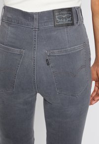 Primer plano de una persona que lleva unos jeans grises de Levi's, mostrando los bolsillos traseros, la costura y la etiqueta de cuero de Levi Strauss & Co.