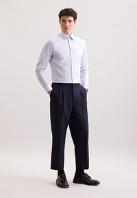 Niebiesko-biała koszula w kratę z długim rękawem, zestawiona z granatowymi spodniami plisowanymi i czarnymi butami, stojąca na jasnym tle.