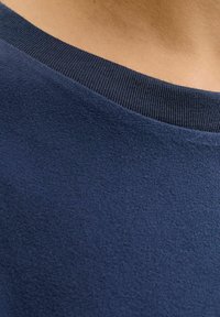 Pull-over en polaire bleu marine, présentant une surface texturée et un col à côtes, conçu pour le confort avec une esthétique minimaliste.