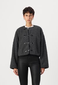 Veste texturée gris foncé avec une coupe carrée, des manches surdimensionnées et des fermetures à bascule. Assortie à un pantalon noir élégant.